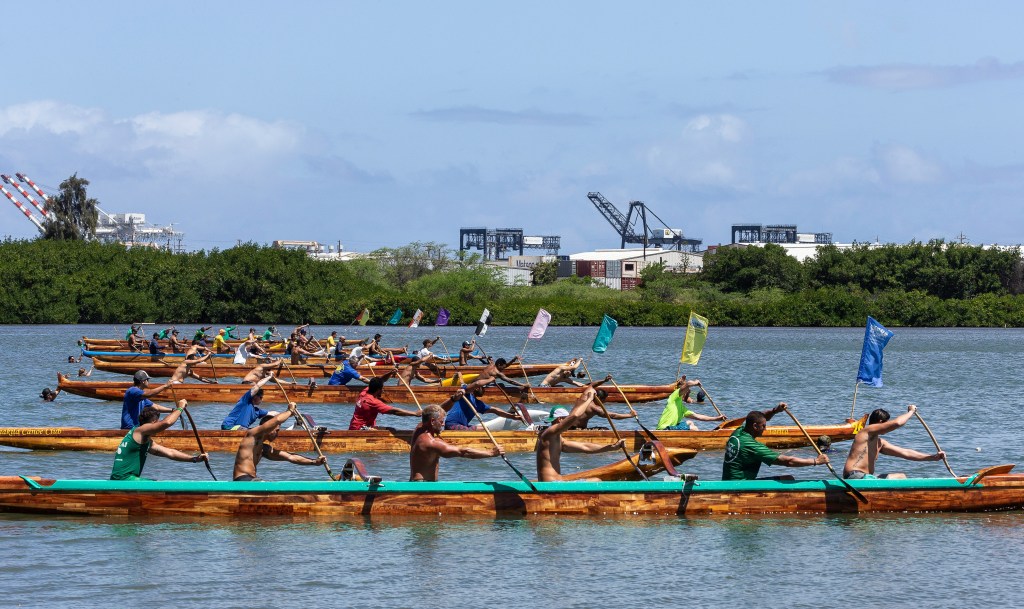 Several boats at the start line ready to race, paddlers at the ready